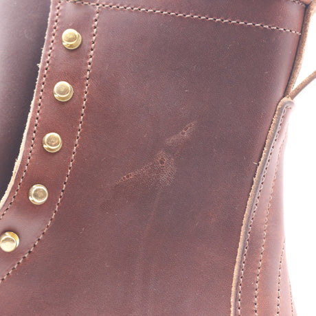Close-up of a brown leather lace-up boot showing gold eyelets and stitching with minor surface imperfections