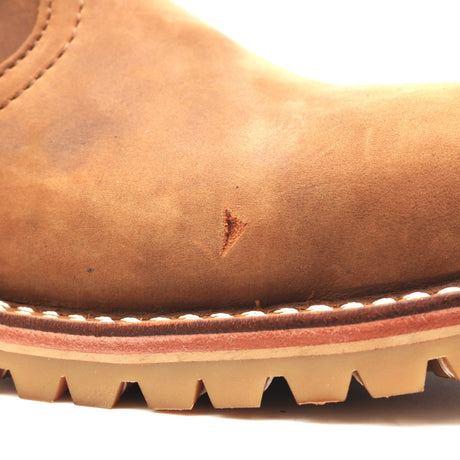 Close-up of a brown leather boot toe showing a small scratch defect white welt stitching and a lugged sole