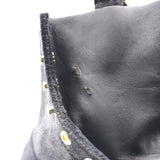 Close-up detail of a black leather garment, showing the texture of the leather, a black velvet trim with gold-tone metal studs, and a white background.