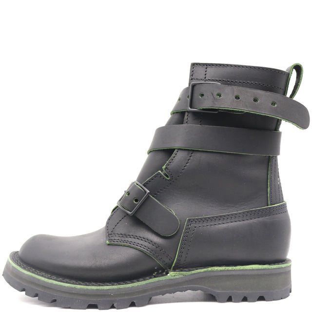 A black leather ankle boot with multiple adjustable straps and a rugged sole, featuring a thin green contrast stitch and green trim along the sole.