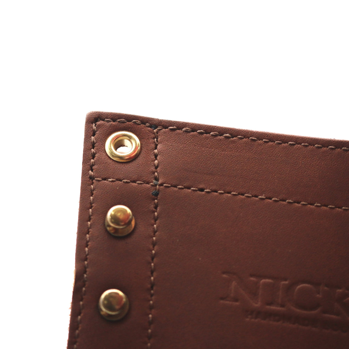 Close-up of a brown leather product corner with brass-tone rivets and an embossed 'NICK' logo on a white background.