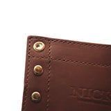 Close-up of a brown leather product corner with brass-tone rivets and an embossed 'NICK' logo on a white background.