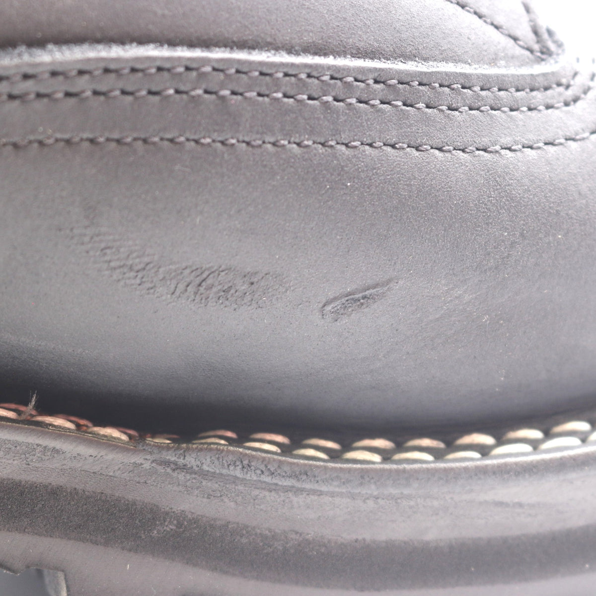 Close-up of a dark gray leather shoe upper with visible scuffing and scratches on the side, showing stitching details.