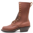 A brown leather mid-calf boot with gold-tone metal eyelets and studs, a low stacked heel, and a pull loop, shown from a side profile on a white background. The brand name 'NICKS' is embossed on the side.