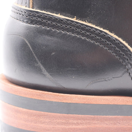 Close-up of a black leather boot showing the heel area with stitching, a tan outsole edge, and a brown and black layered sole.
