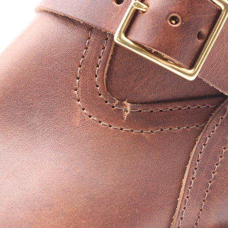 Close-up of a brown leather boot strap with a brass buckle and visible stitching.