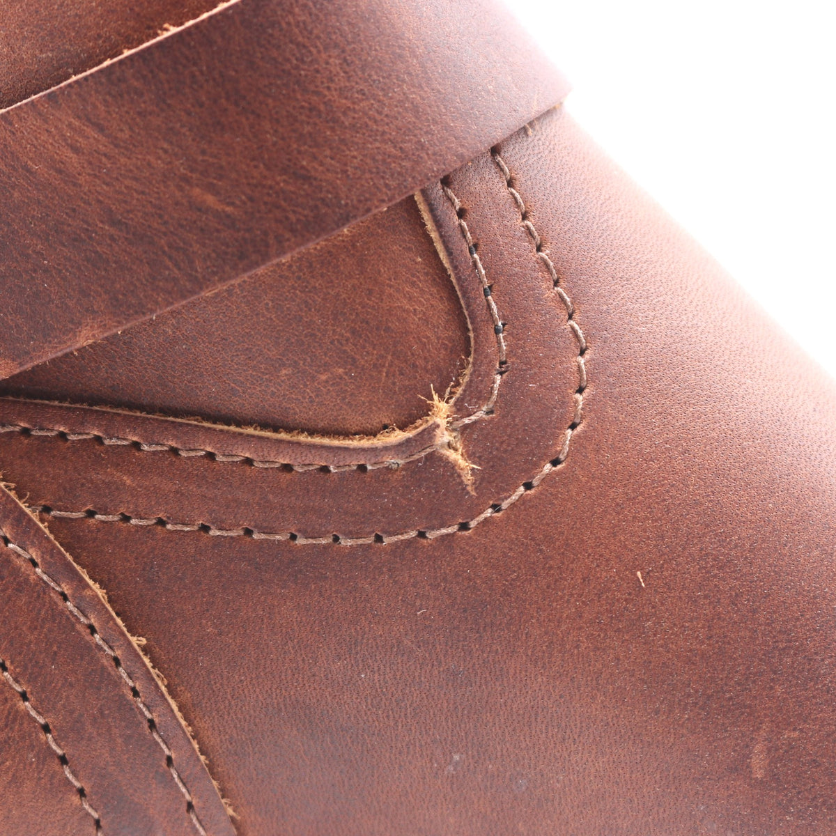Close-up of a brown leather boot showing the texture of the leather, stitching, and a small visible fly on the side.