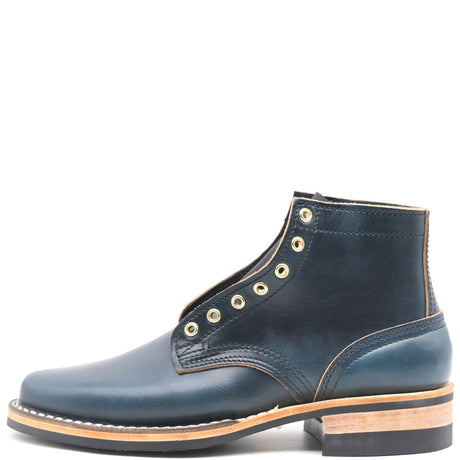 A dark navy blue leather ankle boot with gold-tone metal eyelets, a stacked wood-and-leather heel, and white contrast stitching, shown from a side profile on a white background.