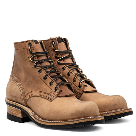 A pair of rugged lace-up ankle boots in distressed tan leather, featuring dark brown laces, metal eyelets, stacked wood-look heels, and black soles, shown on a clean white background.